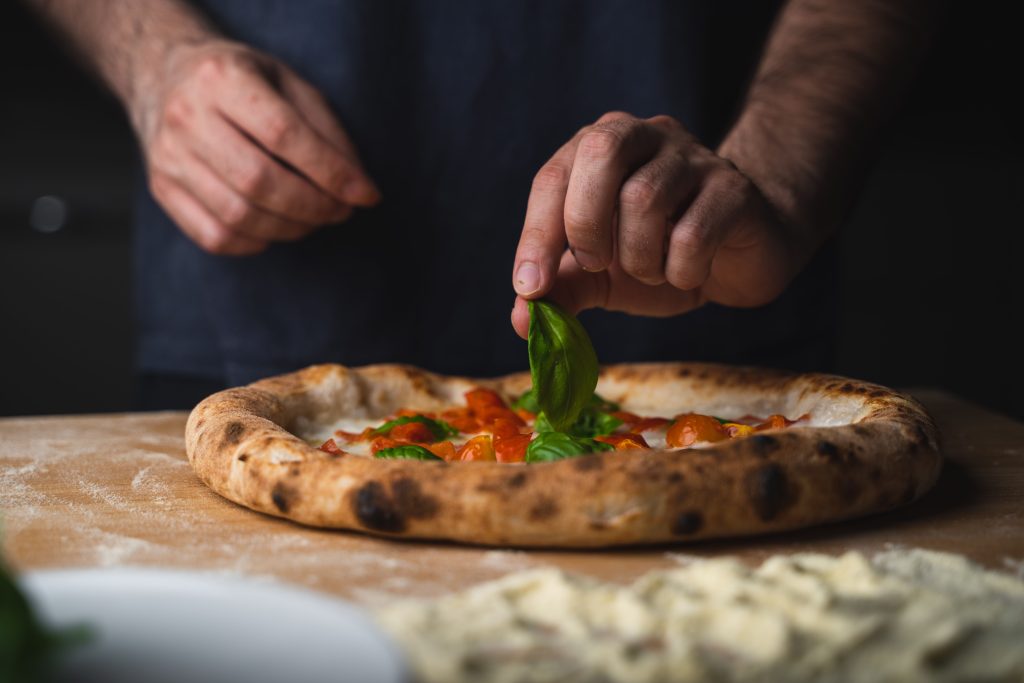 man placing basil freshly baked pizza